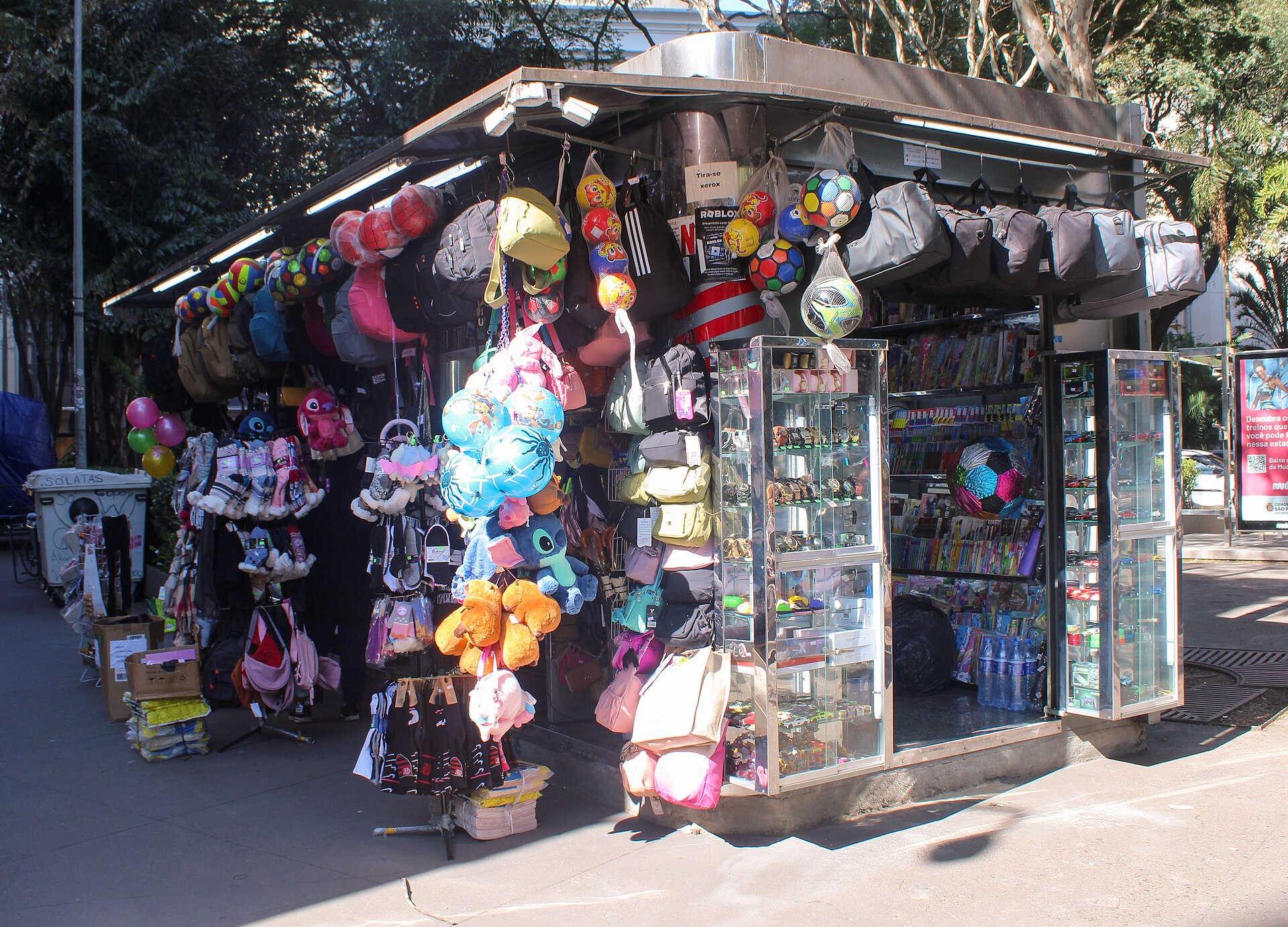 Banca de jornal na calçada da Avenida Paulista, cheia de bolas, mochilas, pelúcias e revistas